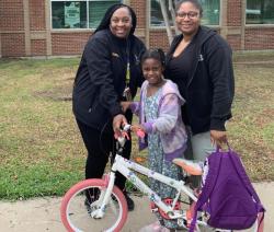 2 adults stand next to girl with new bike