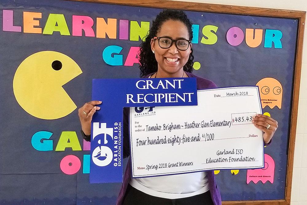 Grant recipient, Tameko Brigham, holds up her GEF check.