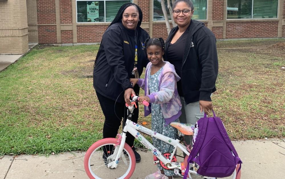 2 adults stand next to girl with new bike